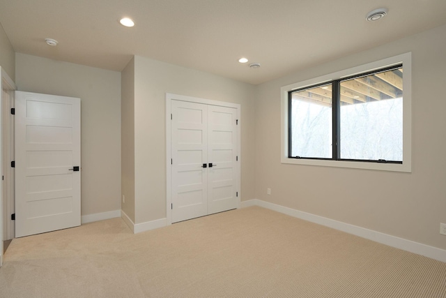 unfurnished bedroom featuring a closet, recessed lighting, light colored carpet, and baseboards