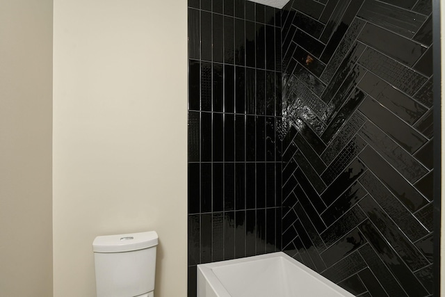 full bathroom featuring tiled shower and toilet