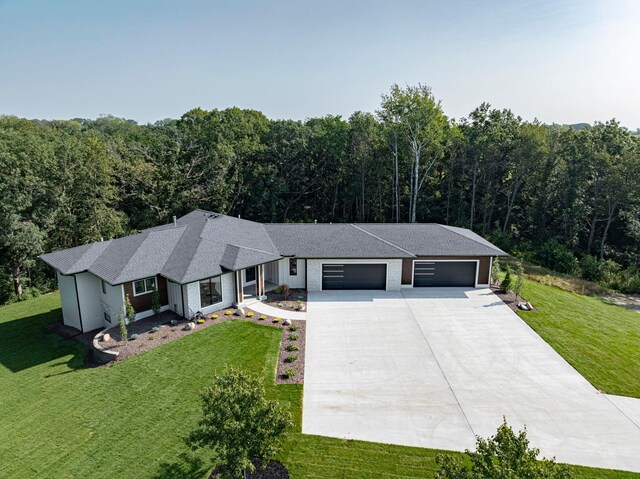 view of front of house with driveway, a forest view, a front yard, a shingled roof, and a garage