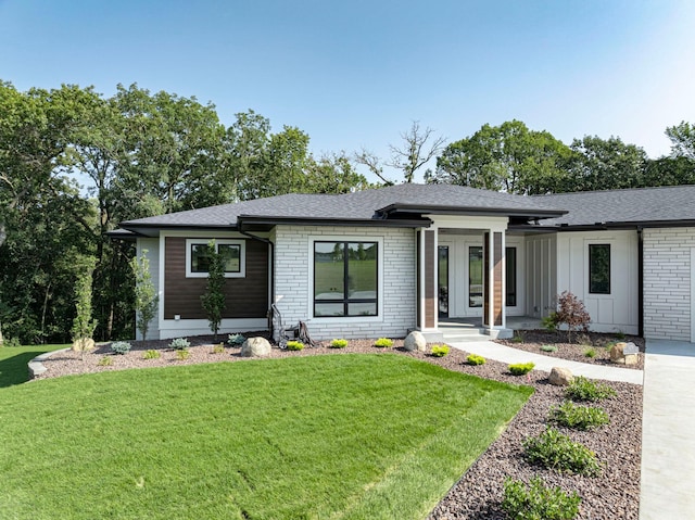 view of front of property with brick siding, board and batten siding, a front lawn, and roof with shingles