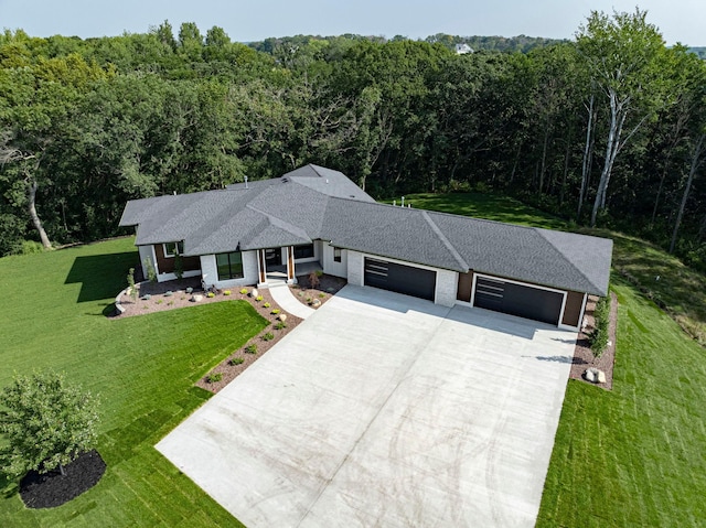 view of front of house featuring an attached garage, a view of trees, driveway, and a front yard