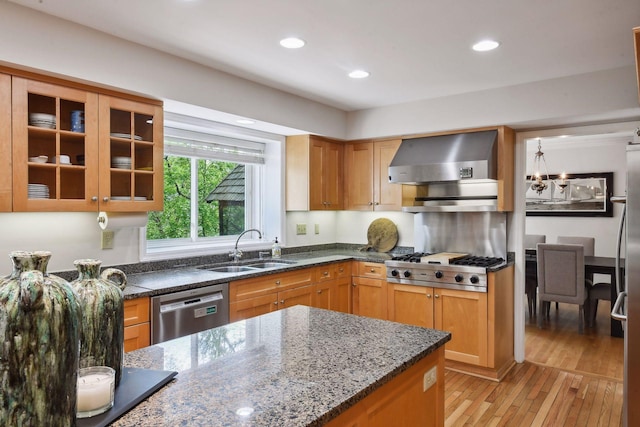 kitchen featuring wall chimney range hood, dark stone countertops, sink, light hardwood / wood-style flooring, and stainless steel appliances