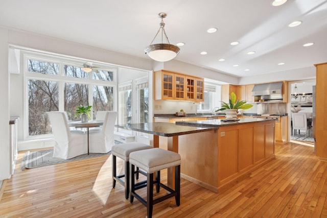 kitchen featuring pendant lighting, dark stone counters, wall chimney exhaust hood, and a kitchen island