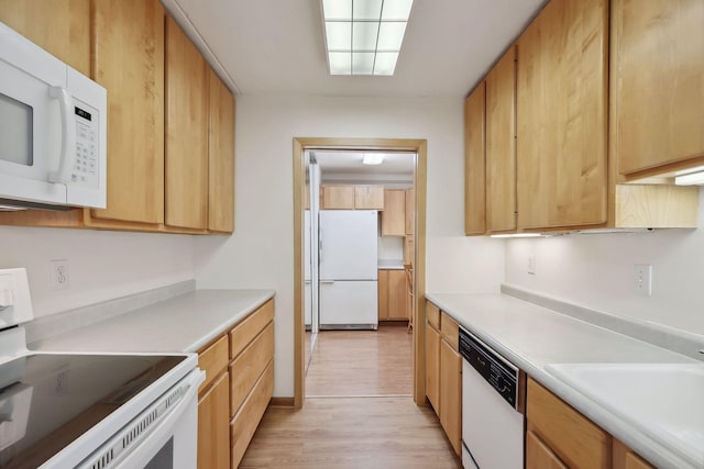 kitchen featuring light wood finished floors, light brown cabinetry, light countertops, white appliances, and a sink