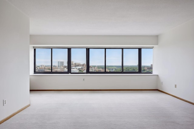 carpeted spare room featuring a textured ceiling, a view of city, and baseboards
