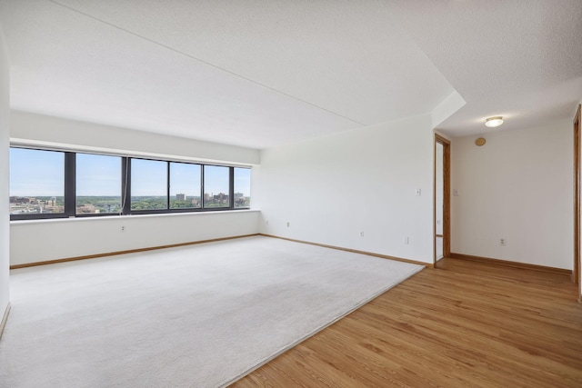 unfurnished room featuring light wood-style flooring, light colored carpet, baseboards, and a textured ceiling
