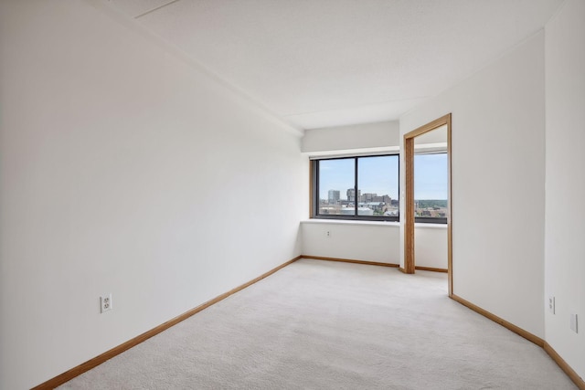 spare room featuring light carpet, a view of city, and baseboards