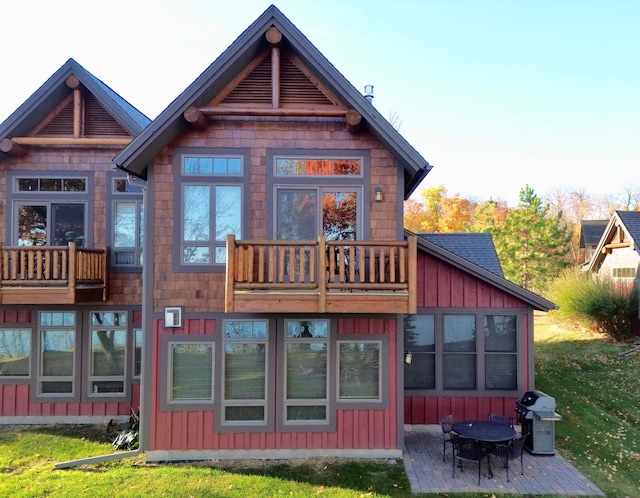 rear view of property featuring a patio, a yard, and a balcony