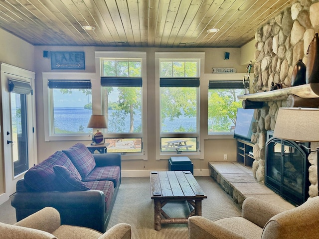 living room with a stone fireplace, wood ceiling, carpet floors, and a water view