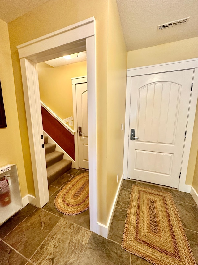 doorway with a textured ceiling and dark tile patterned flooring