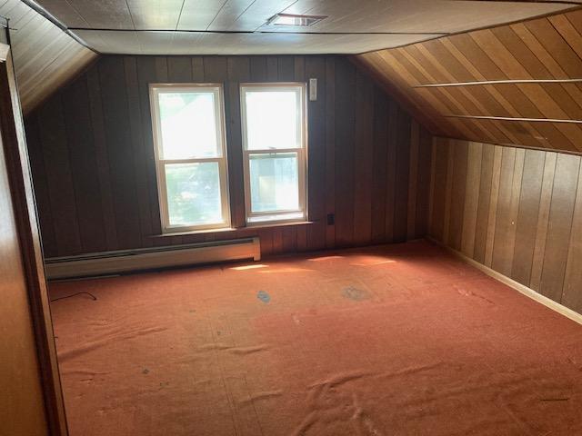 bonus room featuring carpet floors, a baseboard radiator, wood walls, and vaulted ceiling