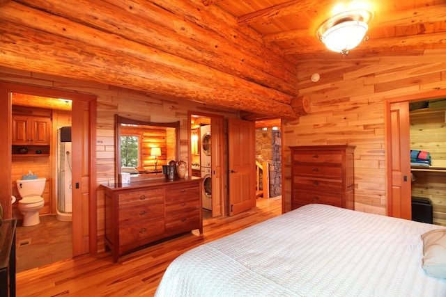 bedroom with wood-type flooring, connected bathroom, wood walls, wood ceiling, and stacked washer and dryer