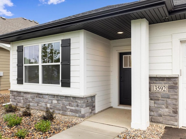 view of exterior entry with stone siding and roof with shingles