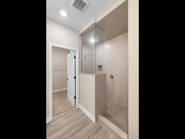 bathroom featuring wood finished floors, visible vents, baseboards, a spacious closet, and walk in shower