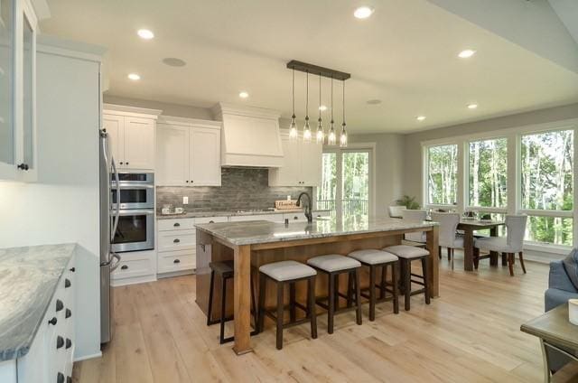 kitchen featuring light hardwood / wood-style floors, a center island with sink, white cabinetry, custom exhaust hood, and hanging light fixtures