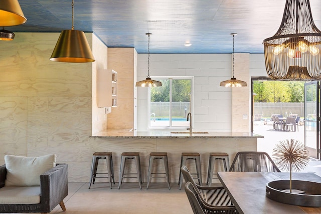 kitchen with a kitchen bar, hanging light fixtures, light stone counters, and sink