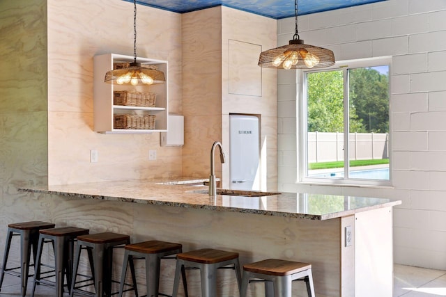 kitchen with hanging light fixtures, a kitchen bar, light stone counters, and a healthy amount of sunlight