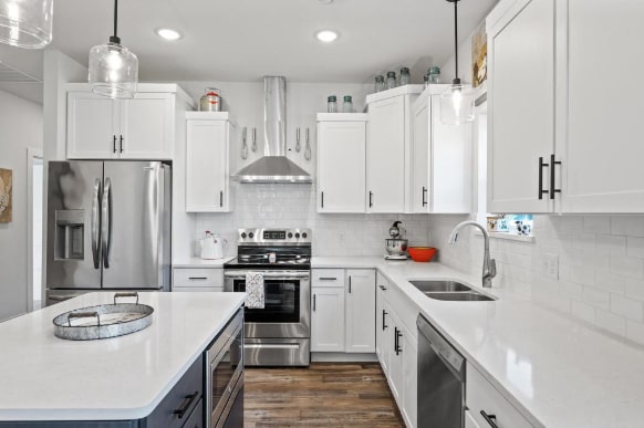 kitchen featuring dark hardwood / wood-style floors, hanging light fixtures, wall chimney range hood, sink, and appliances with stainless steel finishes