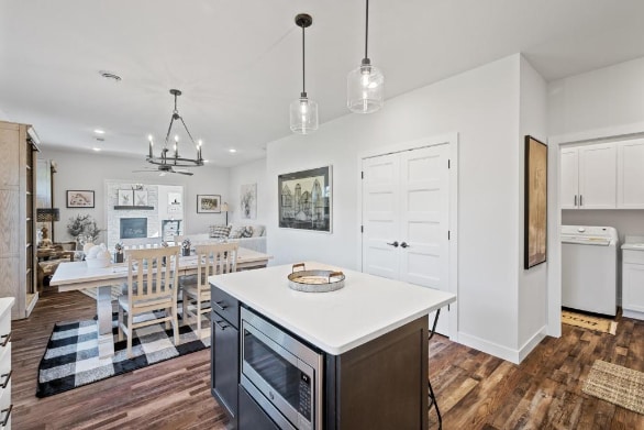 kitchen featuring dark wood-type flooring, hanging light fixtures, stainless steel microwave, and washer / clothes dryer