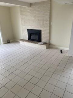 unfurnished living room featuring beamed ceiling, a brick fireplace, and light tile patterned floors