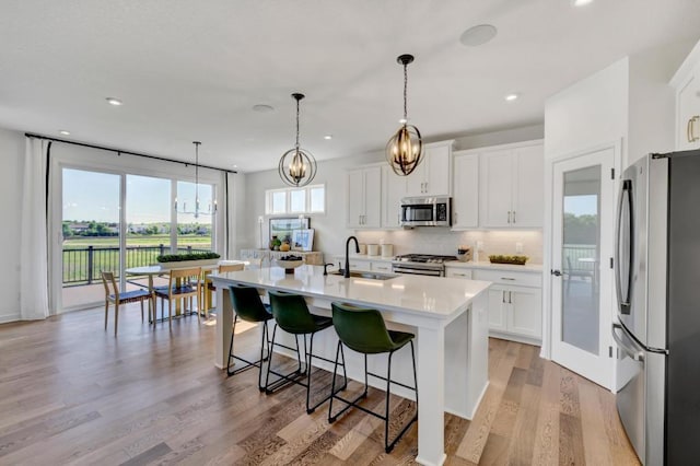 kitchen with white cabinetry, a center island with sink, appliances with stainless steel finishes, hanging light fixtures, and sink