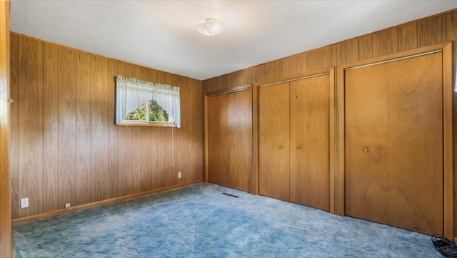 unfurnished bedroom featuring wood walls, light carpet, and two closets