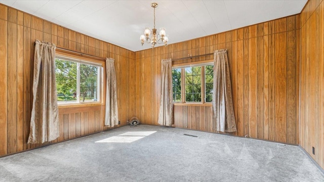 carpeted empty room featuring an inviting chandelier and wooden walls