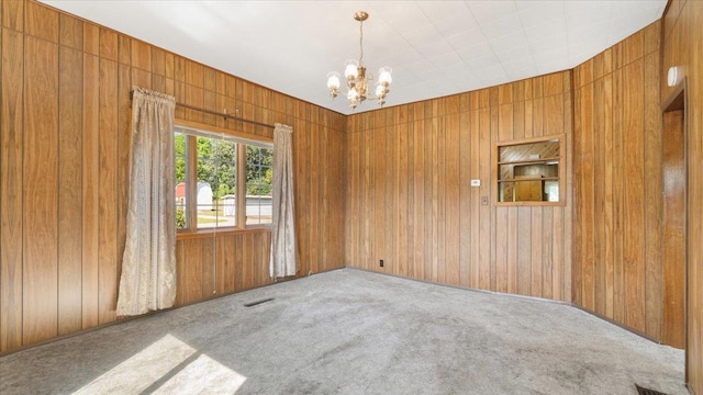 carpeted spare room featuring wooden walls and a chandelier