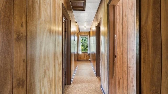 hall with light colored carpet and wooden walls