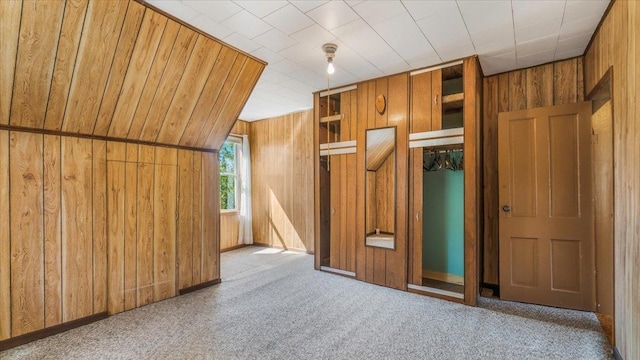 unfurnished bedroom featuring lofted ceiling, carpet flooring, a closet, and wooden walls