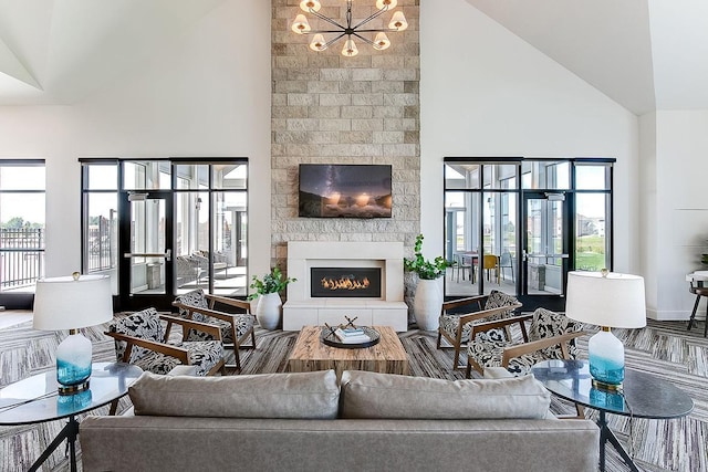 living room with french doors, wood-type flooring, an inviting chandelier, high vaulted ceiling, and a fireplace