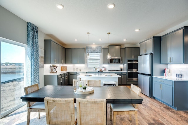 kitchen featuring stainless steel appliances, light hardwood / wood-style flooring, backsplash, decorative light fixtures, and a kitchen island