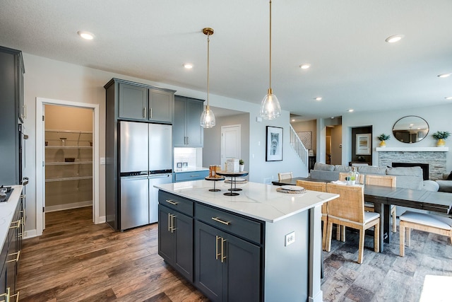 kitchen with dark hardwood / wood-style floors, gray cabinets, stainless steel fridge, light stone countertops, and decorative light fixtures