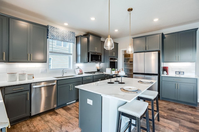 kitchen featuring sink, dark wood-type flooring, decorative light fixtures, a kitchen island, and appliances with stainless steel finishes