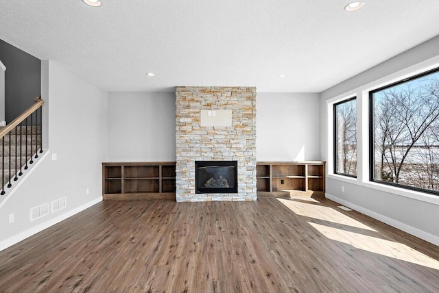 unfurnished living room with a textured ceiling, dark wood-type flooring, and a stone fireplace