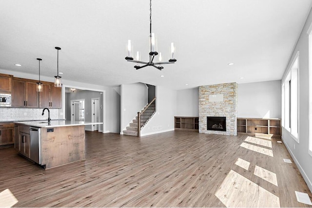 unfurnished living room featuring an inviting chandelier, light hardwood / wood-style flooring, sink, and a stone fireplace