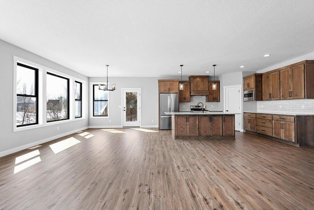 kitchen featuring an island with sink, stainless steel appliances, an inviting chandelier, hanging light fixtures, and dark hardwood / wood-style flooring