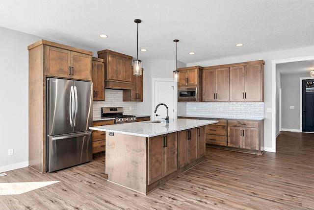 kitchen featuring backsplash, an island with sink, light hardwood / wood-style floors, and appliances with stainless steel finishes