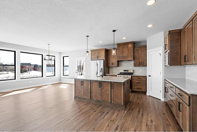 kitchen with backsplash, dark hardwood / wood-style floors, stainless steel appliances, and a kitchen island with sink