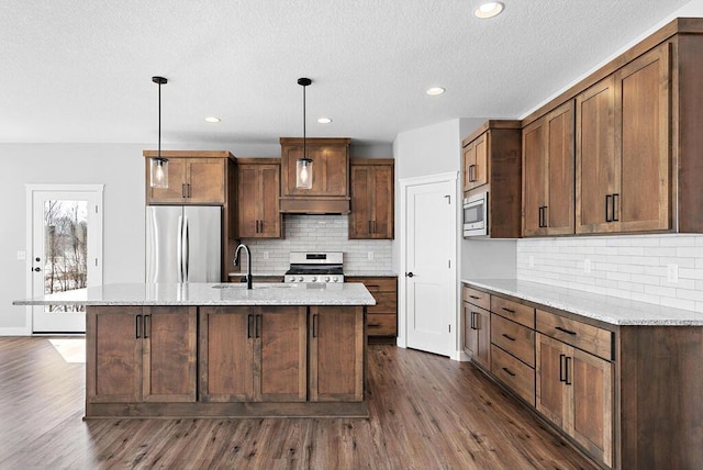 kitchen with appliances with stainless steel finishes, backsplash, decorative light fixtures, a kitchen island with sink, and dark hardwood / wood-style floors