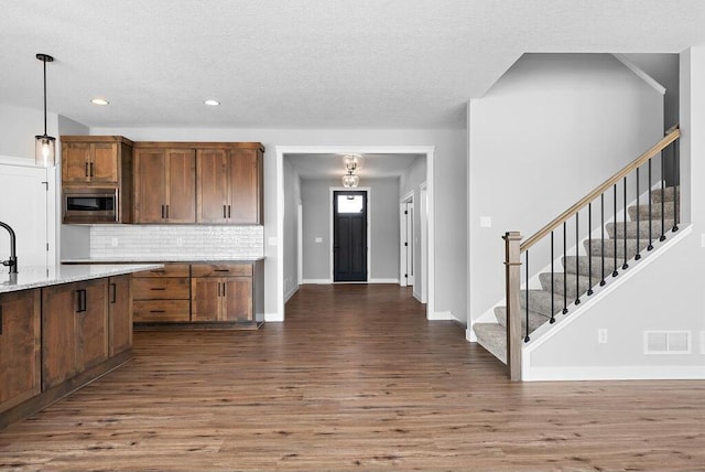 kitchen featuring backsplash, stainless steel microwave, light stone counters, dark hardwood / wood-style flooring, and pendant lighting