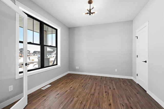 spare room with dark wood-type flooring, an inviting chandelier, and a wealth of natural light