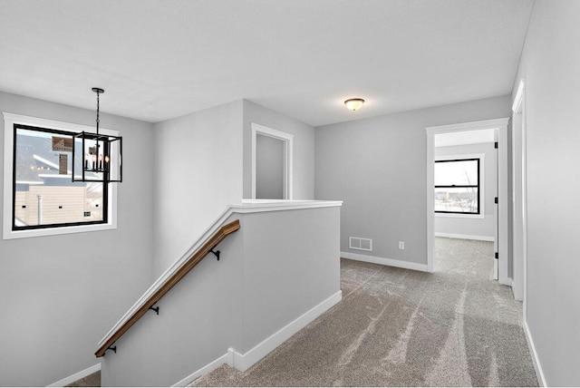 corridor featuring an inviting chandelier and light colored carpet