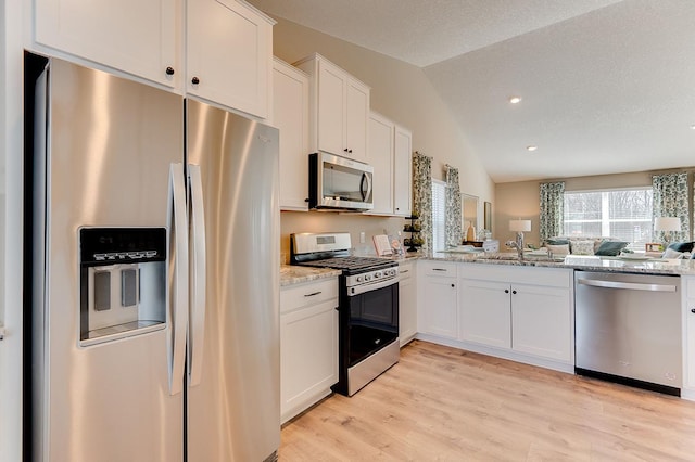 kitchen featuring appliances with stainless steel finishes, lofted ceiling, light stone countertops, and white cabinets