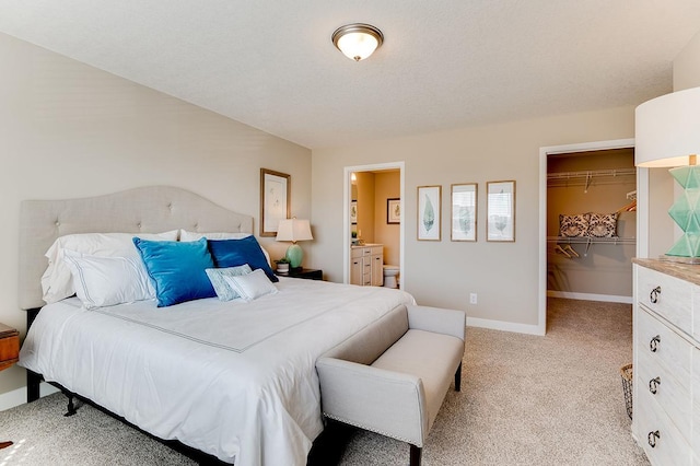 carpeted bedroom with a textured ceiling, a spacious closet, ensuite bathroom, and a closet