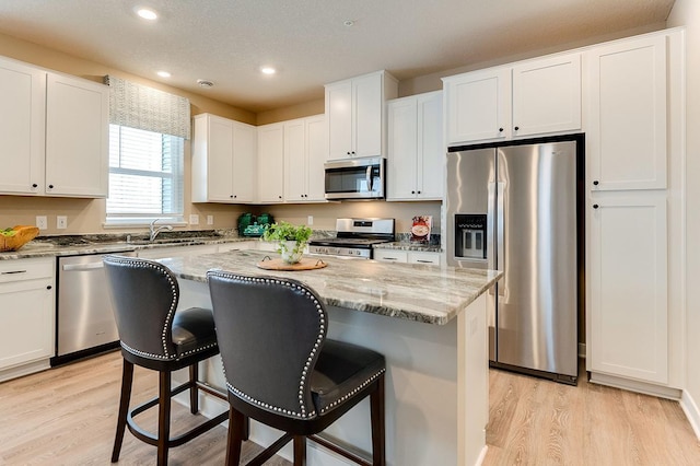 kitchen featuring a kitchen island, white cabinetry, stainless steel appliances, and light hardwood / wood-style flooring