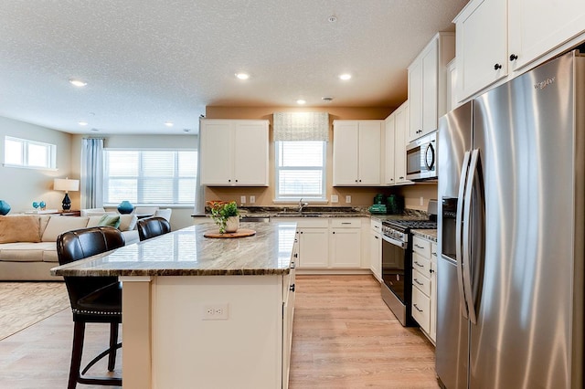 kitchen featuring appliances with stainless steel finishes, a kitchen island, plenty of natural light, and white cabinets