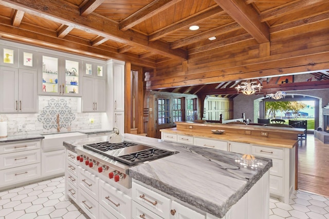 17950 Breezy Point Rd, Woodland, MN 55391 - kitchen with wooden ceiling with exposed beams, a center island, stainless steel gas cooktop, wood walls, and a chandelier
