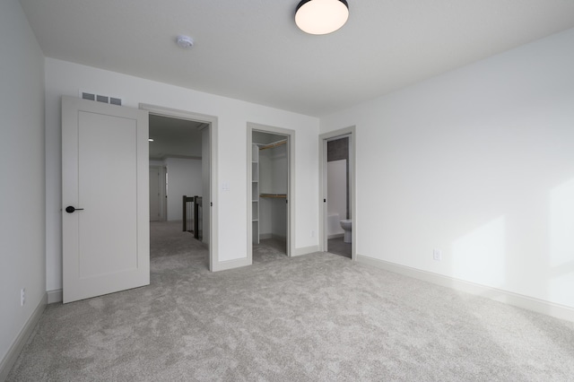 unfurnished bedroom featuring a walk in closet, light colored carpet, and a closet