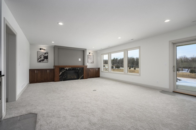 unfurnished living room featuring a wealth of natural light, light colored carpet, and a high end fireplace